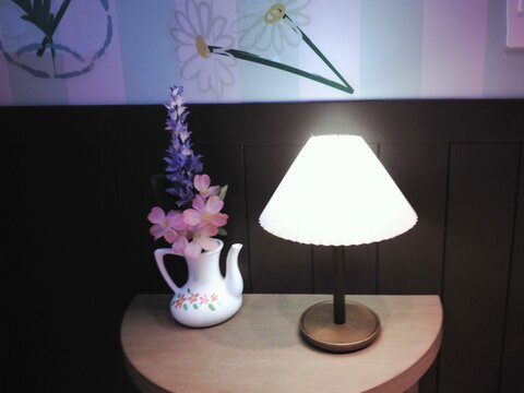 Cozy interior with glowing lamp and flower vase on a table, film photography style.