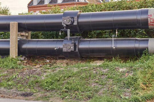 View of large black district heating pipes with industrial valves installed along a grassy embankment in Esbjerg, Denmark.