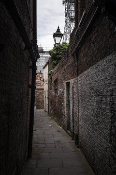 View of a narrow historic alleyway with weathered brick walls, traditional street lamps, and stone paving in York, England, United Kingdom.