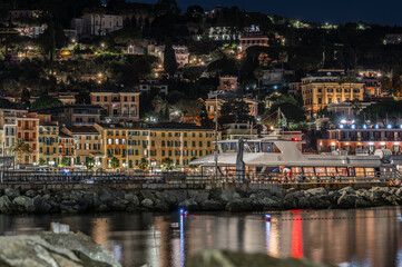 Obraz premium Panoramic night view of illuminated coastal town and hillside houses behind stone breakwater in Santa Margherita Ligure, Italy