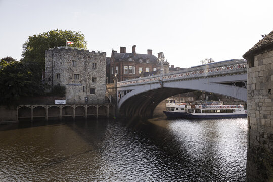 View of Lendal Bridge over the River Ouse with a historic stone tower and a tour boat passing underneath in York, England, United Kingdom.
