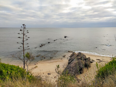A scenic, tranquil coastal landscape featuring rugged cliffs, sandy shores, and serene waters under a cloudy sky. Nobody present in this peaceful, natural setting, evoking stillness and wonder.