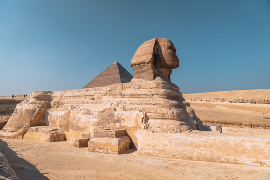 View of the Great Sphinx of Giza with the Great Pyramid of Giza in the background under a clear blue sky in Al Haram, Giza Governorate, Egypt.