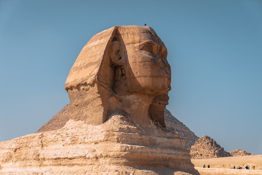 View of the Great Sphinx of Giza with the Pyramid of Khafre in the background under a clear blue sky in Al Haram, Giza Governorate, Egypt.