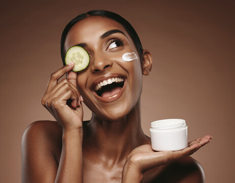 Happy Woman with Glowing Skin Holding a Cucumber Slice and Face Cream Jar