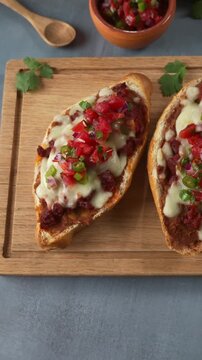 Aerial view of delicious toasted molletes topped with chorizo, melted cheese and fresh pico de gallo on a wooden board