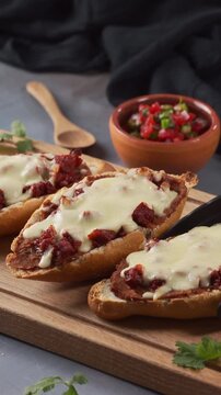 A hand places a piece of mollete with tongs on a wooden board next to more molletes