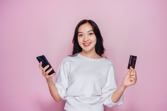 Happy Asian Young Woman Holding Credit Card and Phone Smiling on