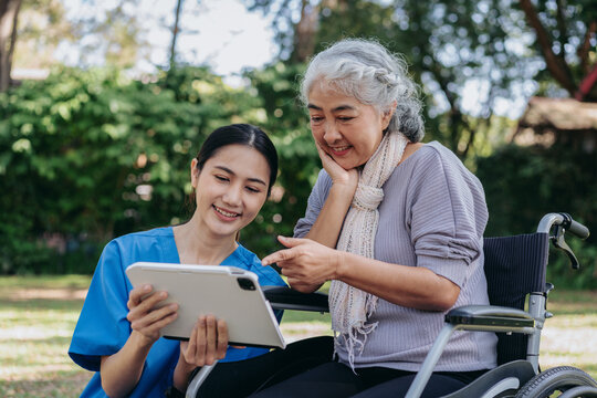 A woman in a blue shirt is helping an older woman in a wheelchair use a tablet