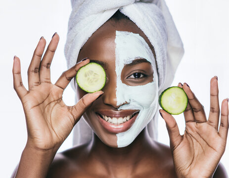 Radiant Black woman with clay face mask holding cucumber slices for skincare