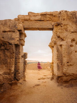 View of a woman in a pink dress standing in the ancient stone doorway of the Amon Temple ruins overlooking the desert landscape in Siwa, Marsa Matrouh Governo, Egypt.