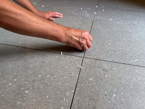 View of a worker installing grey ceramic floor tiles with plastic spacers in Riga, Latvia.