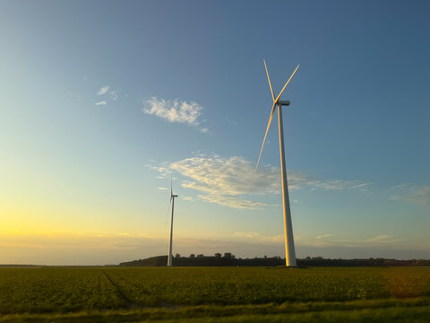 View of two wind turbines standing in a green field during golden hour in Zwolle, Overijssel, Netherlands.