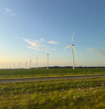 View of a row of wind turbines standing in a green field under a clear blue sky near a road in Zwolle, Overijssel, Netherlands.