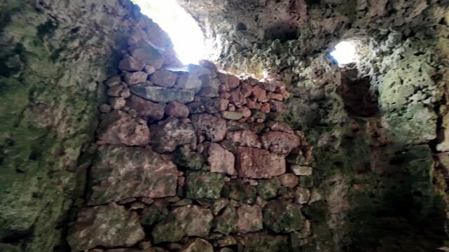 Xemxija, Malta 29.07.2026 - Heritage trail, Roman Baths, shelf like cut in the stone Dark cave walls show rough, textured surfaces. Greenish moss grows on damp, uneven stone. Light filters through nar