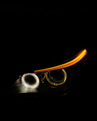 Luxury sedan bi-led headlight with angel eyes close up in dark. Stylish car optics with glowing rings and orange daytime running lights turned on black background. Modern car light, automotive design. © Dmitry Presnyakov