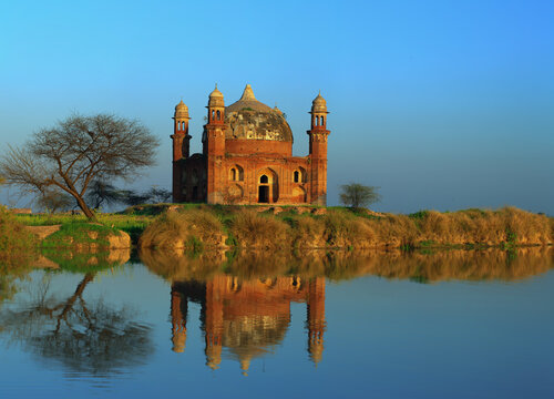 View of the historic Shrine of Abdul Nabi, also known as Maqbra Di Kotli, reflected in the calm water at sunset in Kotli Maqbara, Punjab, Pakistan.