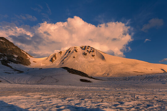 View of Deosai National Park, Burji La top, featuring snow-covered mountain slopes illuminated by golden hour light under a dramatic cloudy sky Skardu, Gilgit Baltistan, Pakistan.