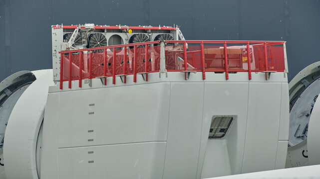 View of wind turbine nacelles with red safety railings and cooling fans stored in the harbor area in Esbjerg, Syddanmark, Denmark.