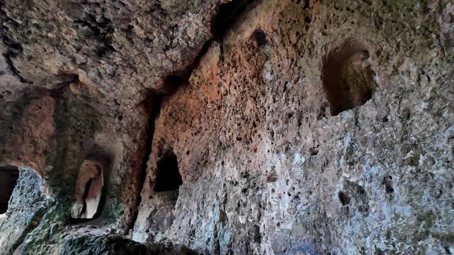 Xemxija, Malta 29.07.2026 - Heritage trail, Roman Baths, shelf like cut in the stone Dark cave walls show rough, textured surfaces. Greenish moss grows on damp, uneven stone. Light filters through nar