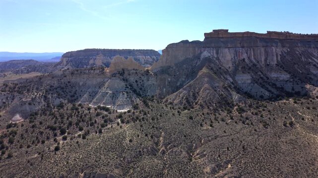 Aerial drone footage of Utah Scenic Byway 12 revealing dramatic desert canyon formations with layered sedimentary cliffs and scattered juniper trees across arid terrain under clear blue sky.
