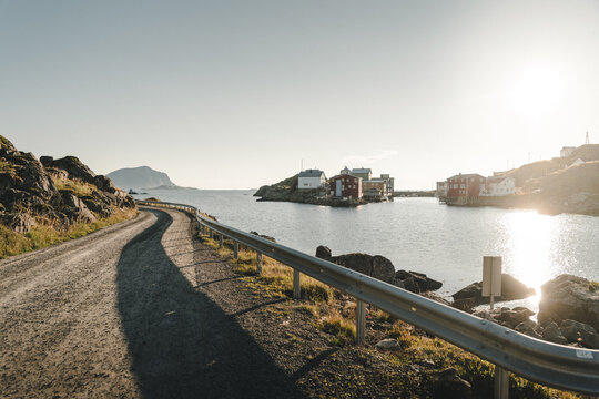 View of the historic fishing village of Nyksund with colorful wooden houses, a winding gravel road in the foreground, and calm sea under bright sunlight in Nyksund, Nordland, Norway.