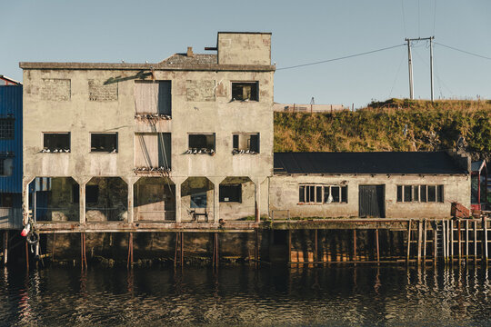 View of the historic weathered concrete building in the old fishing village of Nyksund, with seagulls perched in open windows and a wooden foundation, Nyksund, Nordland, Norway.
