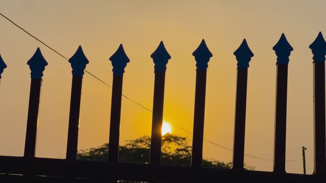 Silhouette of a metal fence at sunset. Dark iron railings against a golden evening sky.