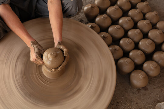 View of a potter shaping a clay vessel on a spinning wheel with rows of finished pottery arranged on the ground in Thatta, Sindh, Pakistan.