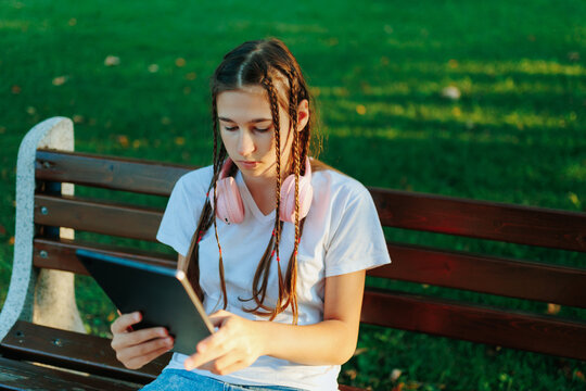 Focused Zoomer schoolgirl using tablet sitting on park bench.