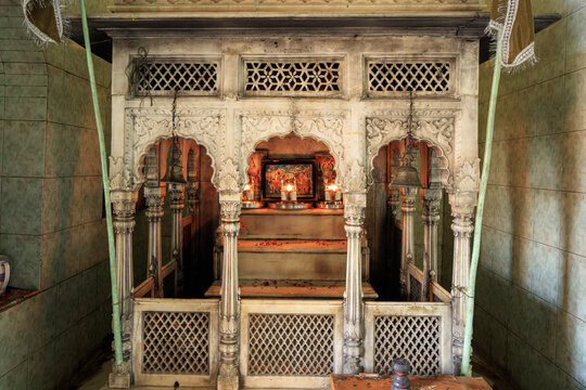 View of the ornate white marble shrine at Udero Lal Mandir with intricate carvings, a religious altar, lit candles, and scattered flower petals in Juma Khan Kalhoro, Sindh, Pakistan.