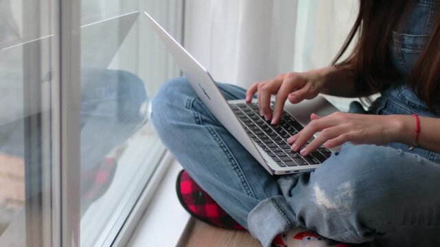Female hands typing on laptop by window, close-up