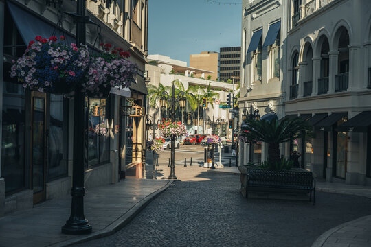 Beverly Hills, California, United States - 15 March 2026: View of Rodeo Drive with luxury storefronts, hanging flower baskets, and cobblestone street under a clear blue sky.