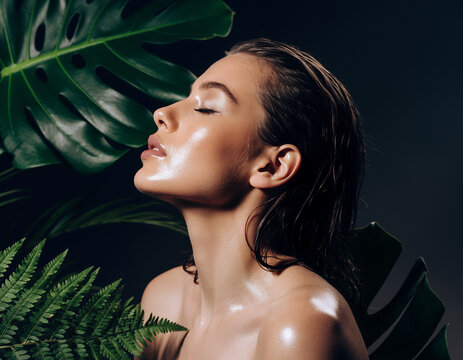 Portrait of a Model with Radiant Wet Skin Surrounded by Green Tropical Leaves