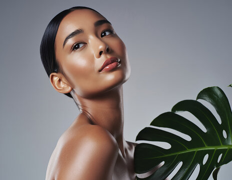 Young elegant woman with flawless complexion holding lush green tropical leaf