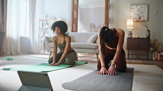 Fitness women stretching yoga mats home. Following workout tutorial tablet.
