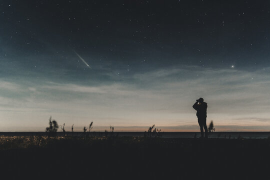 Saxby, Laane maakond, Estonia - 19 October 2024: View of a person silhouetted against the night sky while observing a comet over the Saxby coast, with stars visible above the dark horizon.