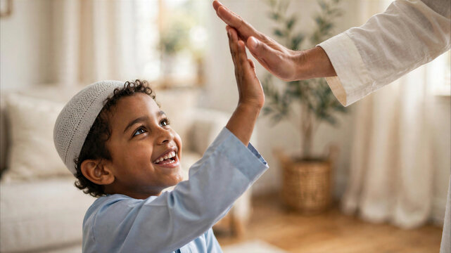 Joyful Muslim boy wearing a kufi giving a high five to his father in a warm and bright living room