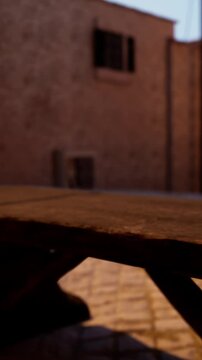 A wooden table sits in a quiet space as evening light casts shadows on the walls. The surrounding area shows textures and details of the setting.