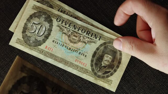 Top view of hands placing vintage 1986 Hungarian 50 forint banknotes with consecutive serial numbers on dark brown background