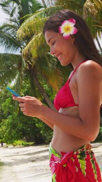 Woman using smart phone on beach on Matira Beach, Bora Bora. Woman on holidays beach vacation wearing pareo in Tahiti, French Polynesia. Vertical video of real woman model without any makeup