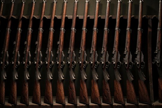 Row of old vintage rifles placed in wooden weapon rack. Antique firearms stand in line at military armory warehouse. Historic guns wait in storage for exhibition museum collection. Retired muskets