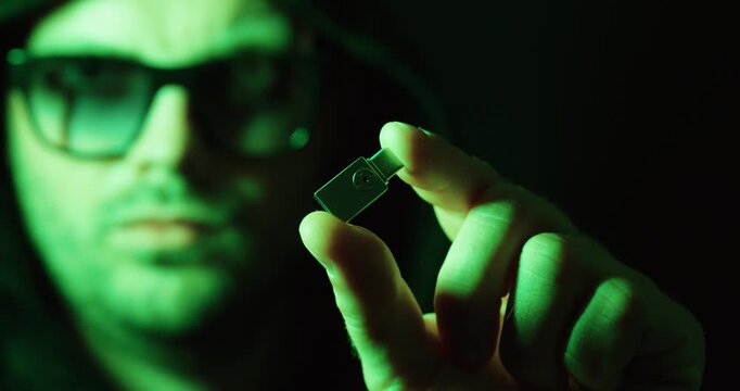 Close-up of a hooded person holding a USB flash drive. Concept of data storage, cybersecurity, digital security, malware, and information technology.
