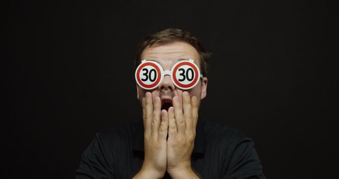 A shocked man wears novelty glasses with the number 30, humorously reacting to turning thirty. Concept of milestone birthdays, aging, adulthood, and life transitions.
