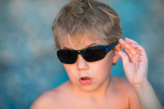 5 year old blond boy in sunglasses gesturing toward the camera.