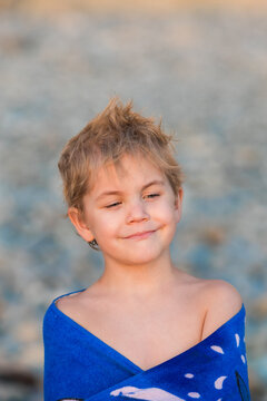 Thoughtful 5 year old boy wrapped in a blue towel on a pebble beach.