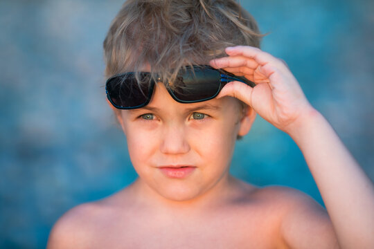 5 year old blond boy in sunglasses gesturing toward the camera.