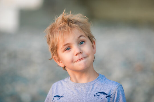 5 year old blond boy in a gray shirt looking away in soft beach light.