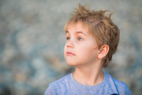 5 year old blond boy in a gray shirt looking away in soft beach light.