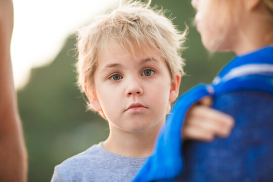 5 year old blond boy with serious expression among blurred beach figures.